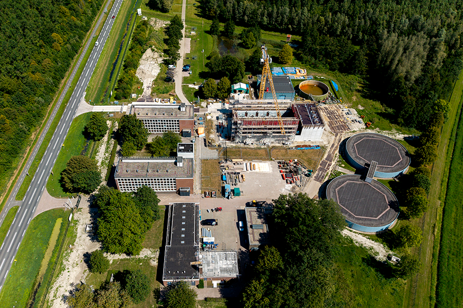 Een grote bouwplaats met winputten, een kraan en een gebouw in aanbouw, gezien vanuit de lucht