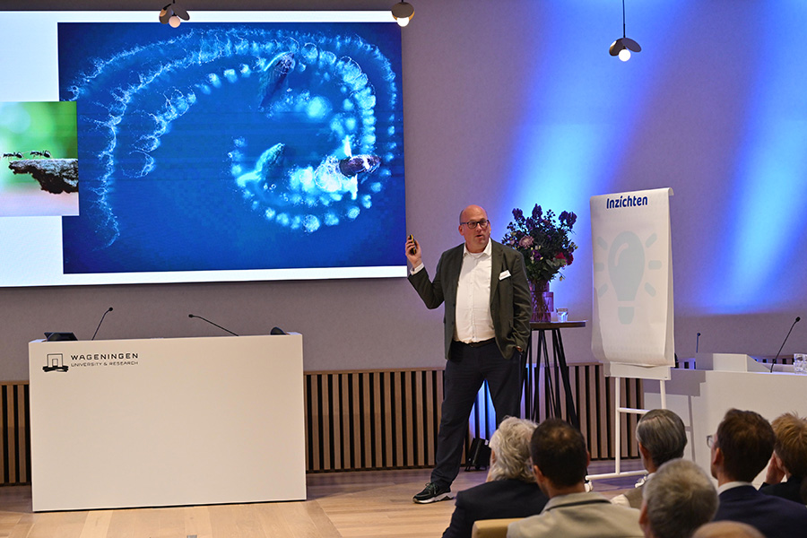  Futuroloog Maurits Kreijveld op podium, wijzend naar een afbeelding op het diascherm.