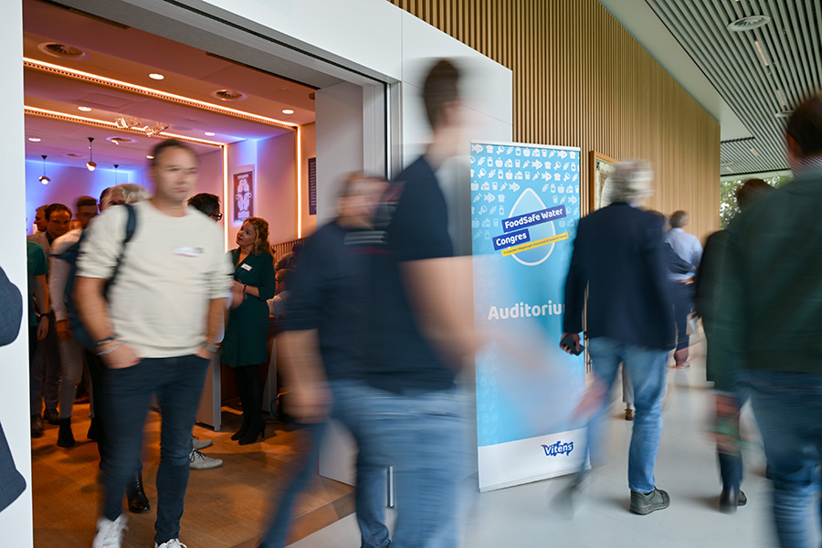 Mensen lopen uit zaal met grote banner FoodSafe Water Congres.