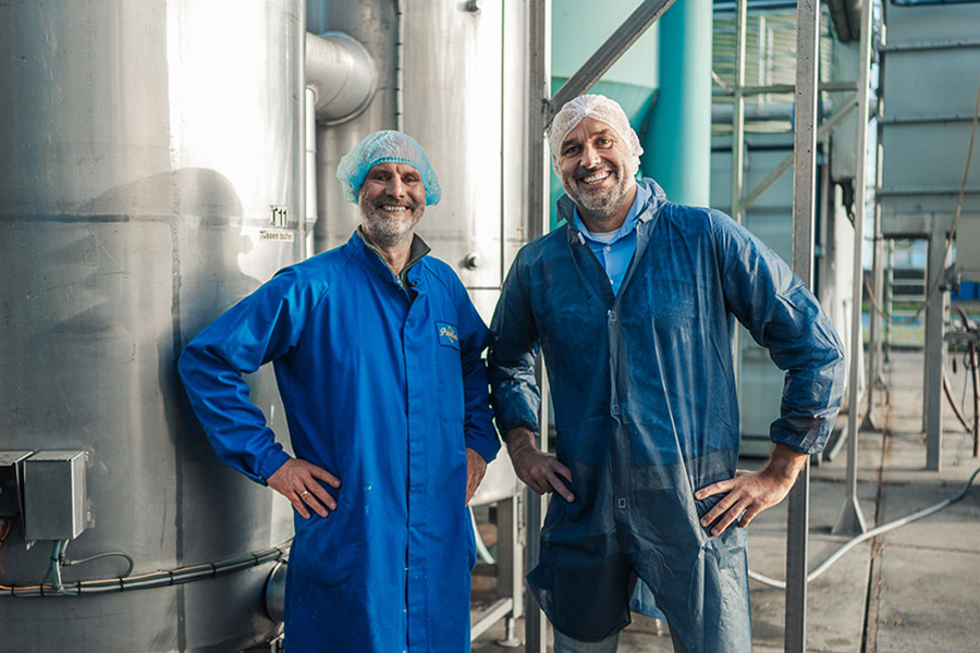 Twee mannen staan met armen in de zij in grote fabriekshal.