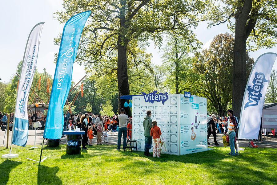 Zonnige foto van de douchekubus op een grasveld met op de achtergrond het Koningsfestival in Enschede