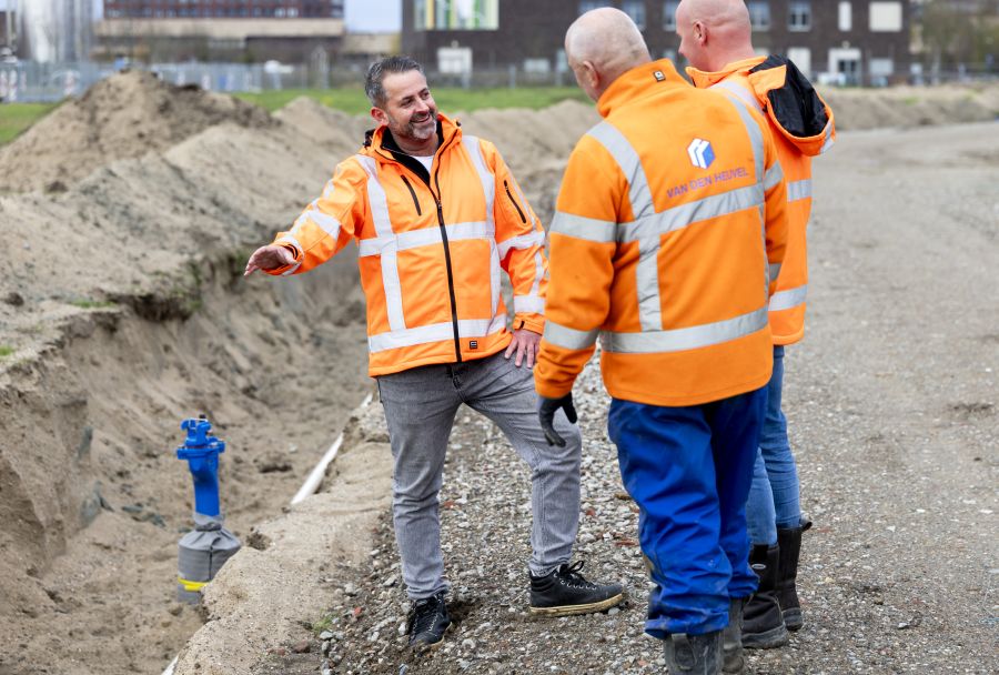 Groep mannen staat bij open sleuf met drinkwaterleiding erin.
