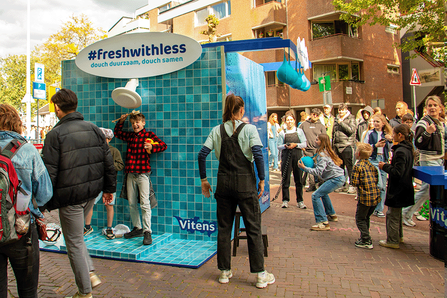 Kinderen poseren in douchekubus en spelen druppelspel op drukke straat tijdens Bevrijdingsfestival in Wageningen