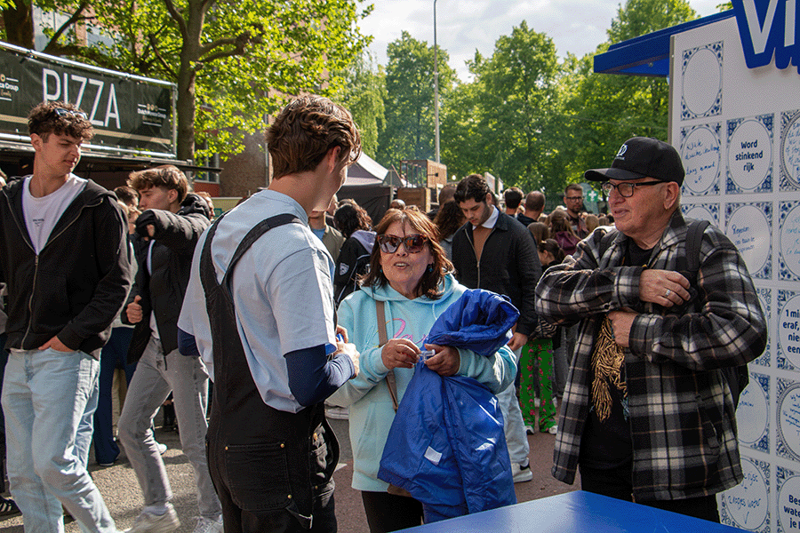 Host voert gesprek met twee bezoekers op drukke straat in Wageningen