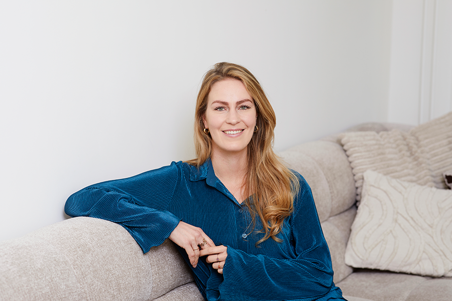 Vrouw met lang blond haar en blauwe blouse zit op beige bank
