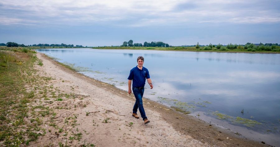 Man loopt langs grote plas water met droge grond