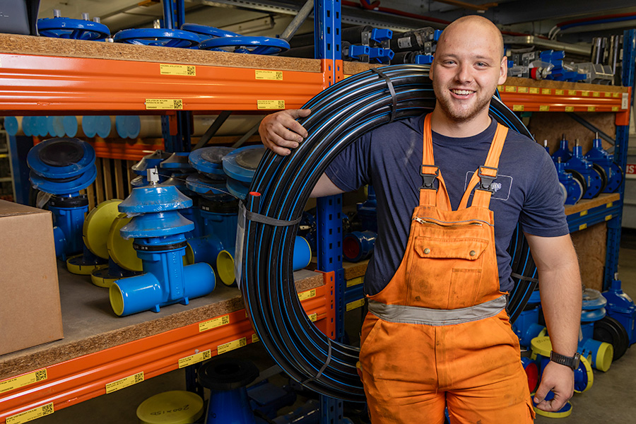 Man met oranje werkbroek en shirt met Vitens-logo staat voor stellingen met technische producten