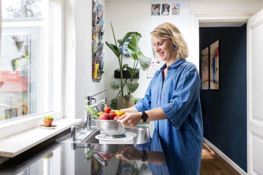 Vrouw vangt water op onder vergiet in gootsteen