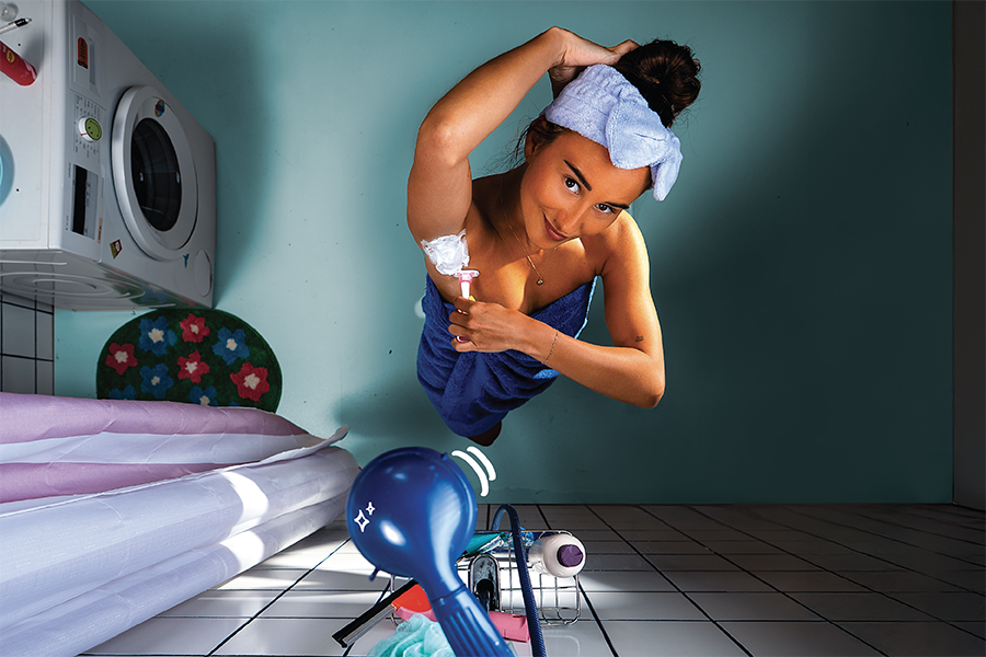 Vrouw met scheermesje staat in rommelige badkamer onder de douche