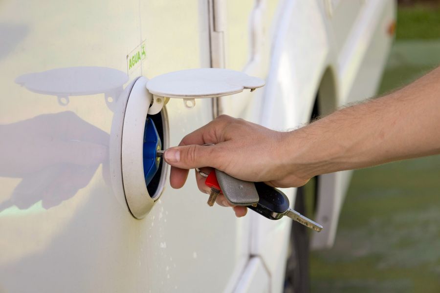 Hand opent klep naar watertank van een camper.