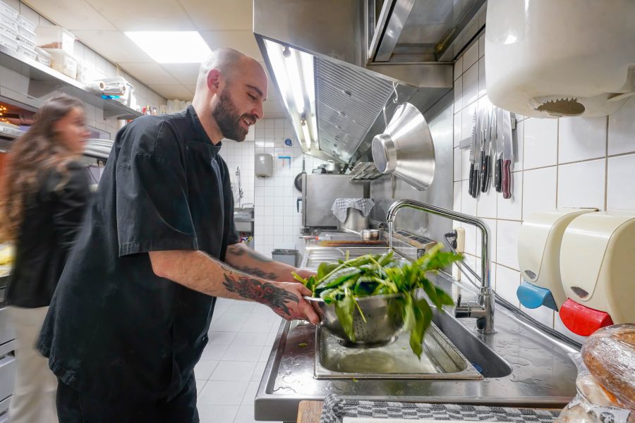 Man staat in de keuken en wast sla